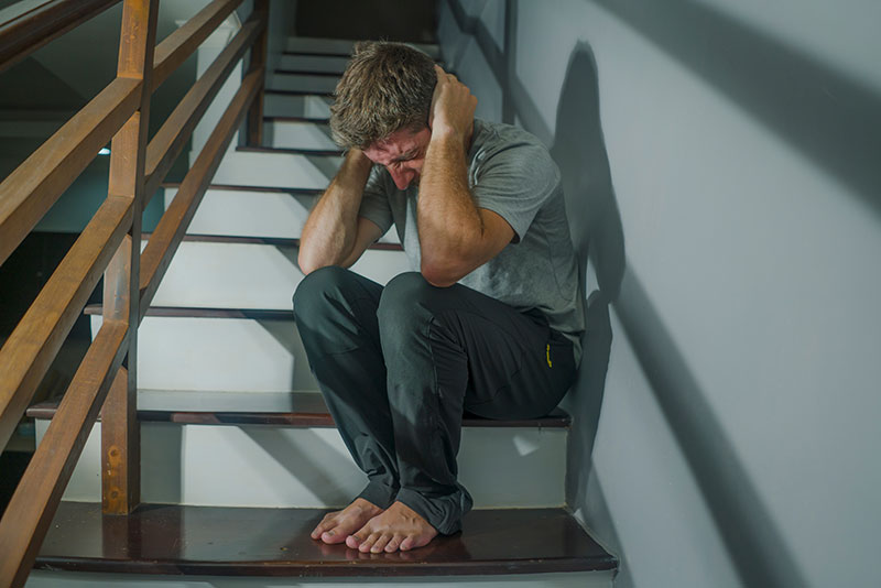 Man sitting on the stairs, head down, with hands on the side of his head signifying his violent experience in a relationship