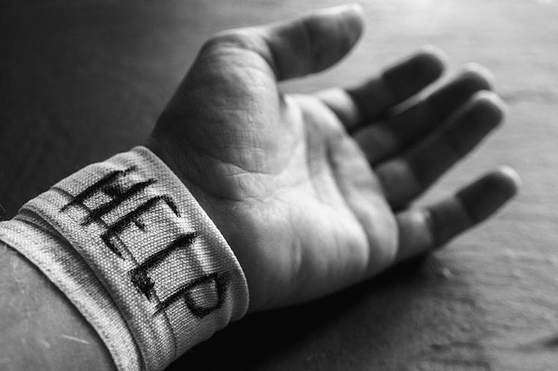 Hand laying on the ground with a bandage around the wrist with the word help on it, as an indication of self-harm